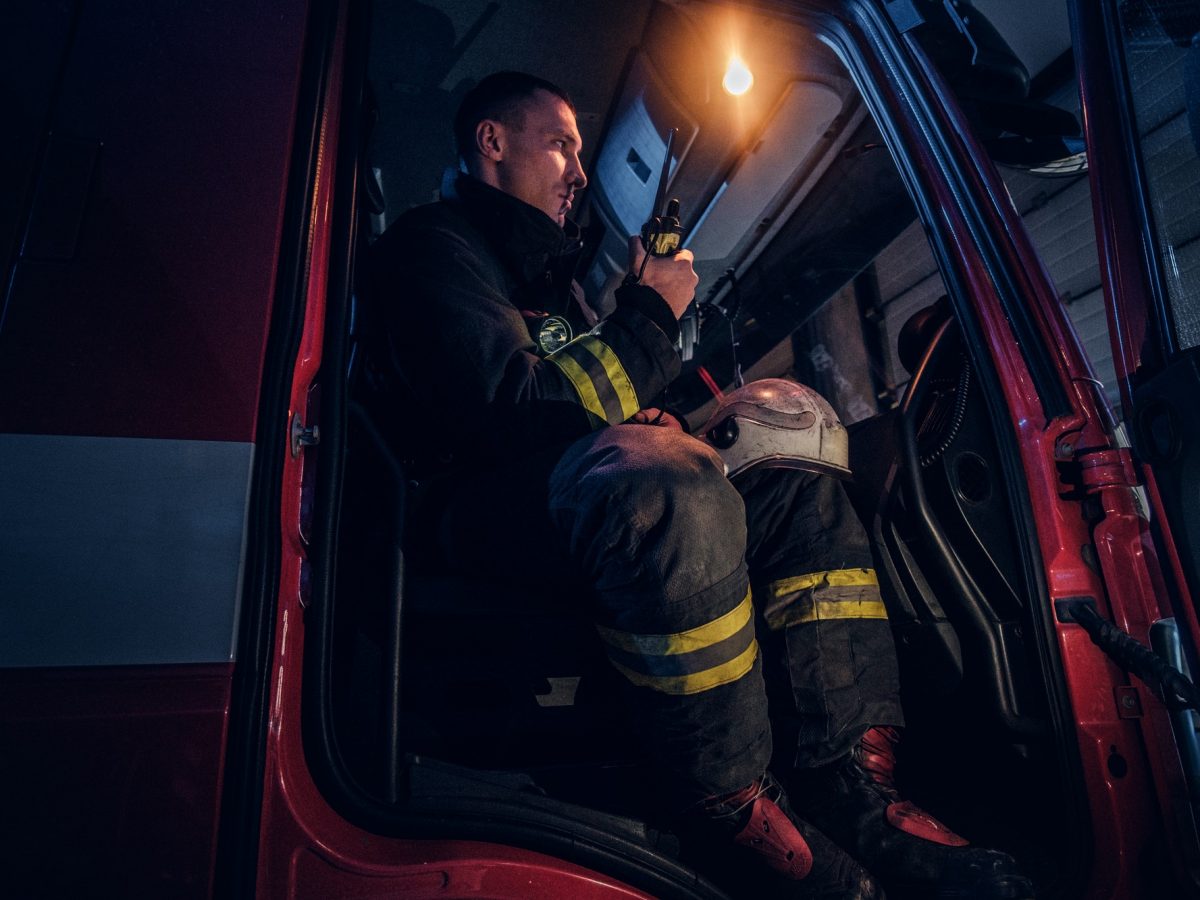 Fireman in a protective uniform sitting in the fire truck and talking on the radio